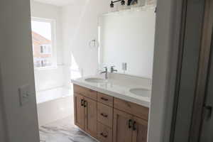 Bathroom with a bath, double vanity, marble finish floor, and a sink