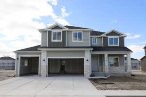 Craftsman-style house featuring a shingled roof, an attached garage, stone siding, board and batten siding, and driveway