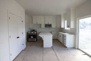 Kitchen featuring range with gas cooktop, stainless steel microwave, a kitchen island, and white cabinets