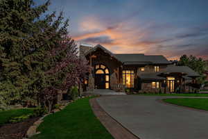 View of front facade with stone siding, curved driveway, a chimney, and a front yard