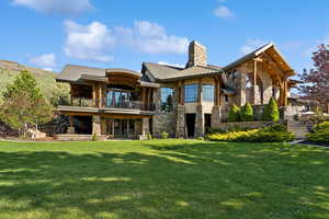 Back of house featuring stone siding, a balcony, a chimney, and a yard