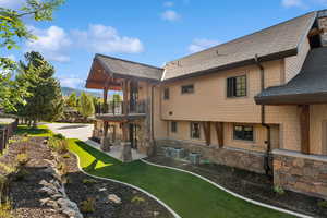 Back of property with a balcony, a patio, a yard, central AC unit, and roof with shingles