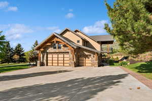 Craftsman-style home featuring stone siding, a balcony, concrete driveway, and a front lawn