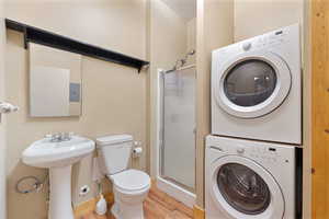 Bathroom featuring estacked washer and dryer, wood finished floors, a shower stall, and toilet