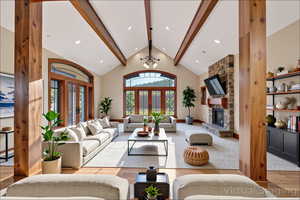 Living area featuring beamed ceiling, plenty of natural light, french doors, wood finished floors, and a stone fireplace