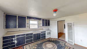 Kitchen with blue cabinetry, a heating unit, a sink, and white range with electric cooktop