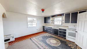 Kitchen featuring dark cabinetry, white electric range oven, a sink, and a healthy amount of sunlight