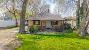Rear view of property featuring a shingled roof, fence, and a lawn