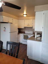 Kitchen featuring white appliances, white cabinets, under cabinet range hood, ceiling fan, and a sink