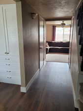 Hallway featuring wood finished floors, a textured wall, and baseboards