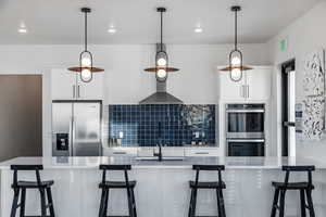 Kitchen featuring white cabinets, decorative light fixtures, wall chimney range hood, stainless steel appliances, and decorative backsplash