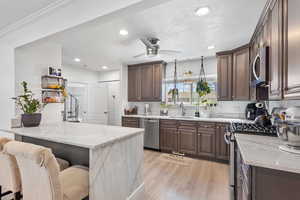 Kitchen with appliances with stainless steel finishes, light stone counters, light wood-style floors, ceiling fan, and a sink