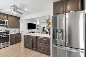 Kitchen featuring light wood-type flooring, dark brown cabinets, recessed lighting, light stone countertops, and stainless steel appliances