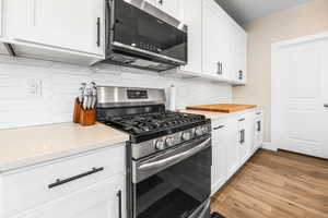 Kitchen with wood finished floors, light countertops, white cabinetry, and stainless steel appliances