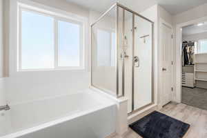 Primary full bath with a bath, a stall shower, wood finished floors, and a spacious closet