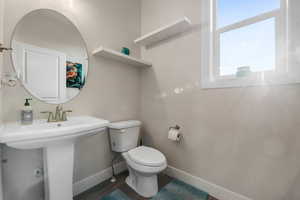 Half bathroom with toilet, wood finished floors, a sink, and baseboards