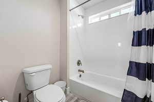 Bathroom with toilet, shower / tub combo, and wood finished floors