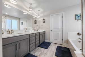 Primary full bathroom featuring a bath, wood finished floors, a sink, double vanity, and baseboards