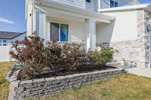 View of side of property with covered porch, fence, and stone siding