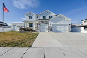 View of front of property with driveway, board and batten siding, stone siding, a front yard, and fence