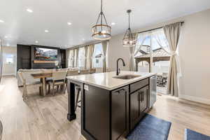Kitchen with an inviting chandelier, light wood-style flooring, light countertops, a center island with sink, and a sink