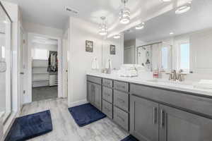 Primary full bath featuring a stall shower, double vanity, a sink, and visible vents