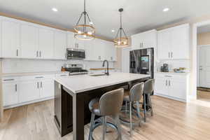Kitchen with tasteful backsplash, appliances with stainless steel finishes, light countertops, a sink, and a center island with sink