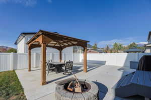 View of patio featuring outdoor dining space, a fenced backyard, a fire pit, and a gazebo