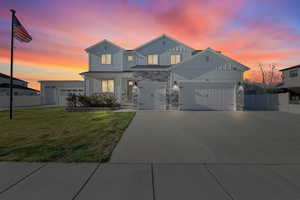 View of front of property featuring stone siding, a garage, a lawn, fence, and concrete driveway