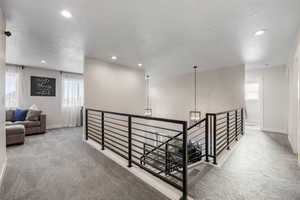 Corridor featuring a chandelier, a textured ceiling, carpet, and an upstairs landing