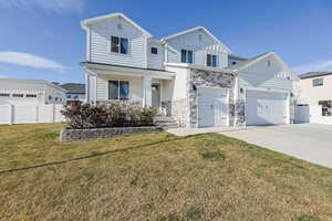 View of front of home with stone siding, board and batten siding, fence, a front lawn, and driveway