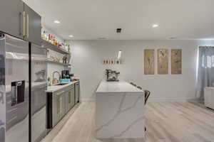 Kitchen with light wood-style floors, stainless steel fridge with ice dispenser, a peninsula, open shelves, and a sink