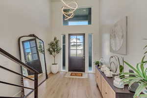 Foyer entrance featuring light wood finished floors, plenty of natural light, an inviting chandelier, and a towering ceiling