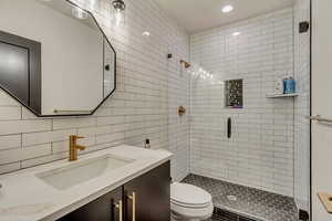 Bathroom featuring vanity, recessed lighting, toilet, a shower stall, and tile walls