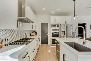 Kitchen featuring decorative light fixtures, a sink, wall chimney range hood, appliances with stainless steel finishes, and light wood-style flooring