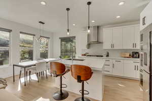 Kitchen featuring light wood-style floors, wall chimney exhaust hood, light countertops, a sink, and decorative backsplash