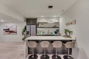 Bar with indoor wet bar, visible vents, a sink, stainless steel fridge, and light wood finished floors