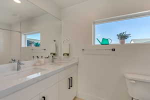 Bathroom featuring a shower, double vanity, a sink, and toilet
