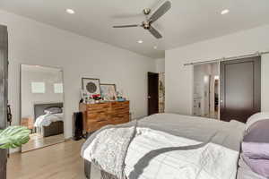 Bedroom featuring light wood-type flooring, a ceiling fan, a barn door, and recessed lighting