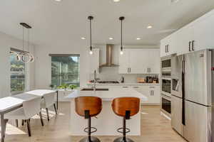 Kitchen with light wood-style flooring, wall chimney range hood, appliances with stainless steel finishes, a sink, and decorative backsplash