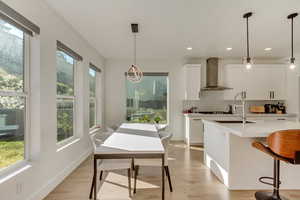 Kitchen with wall chimney exhaust hood, white cabinets, light countertops, a sink, and backsplash