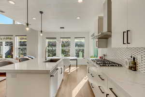 Kitchen with light wood-style floors, wall chimney exhaust hood, tasteful backsplash, appliances with stainless steel finishes, and a sink