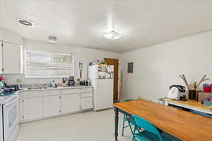 Kitchen with white appliances, a textured ceiling, a sink, and white cabinetry