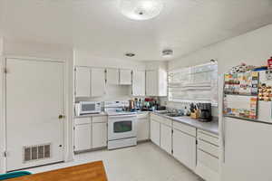 Kitchen featuring visible vents, a sink, white appliances, a textured ceiling, and white cabinetry