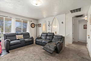 Carpeted living area with arched walkways, a notable chandelier, visible vents, and a textured ceiling