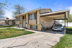 Split foyer home featuring brick siding, a front yard, a carport, and concrete driveway
