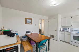 Interior space featuring white appliances, light floors, a textured ceiling, white cabinets, and visible vents
