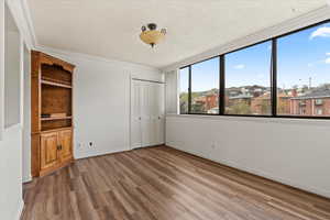 Unfurnished bedroom featuring a closet, a textured ceiling, ornamental molding, and wood finished floors