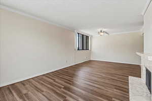 Unfurnished living room with ornamental molding, a fireplace, wood finished floors, and a textured ceiling