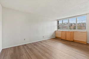 Empty room with a textured ceiling, light wood finished floors, and baseboards